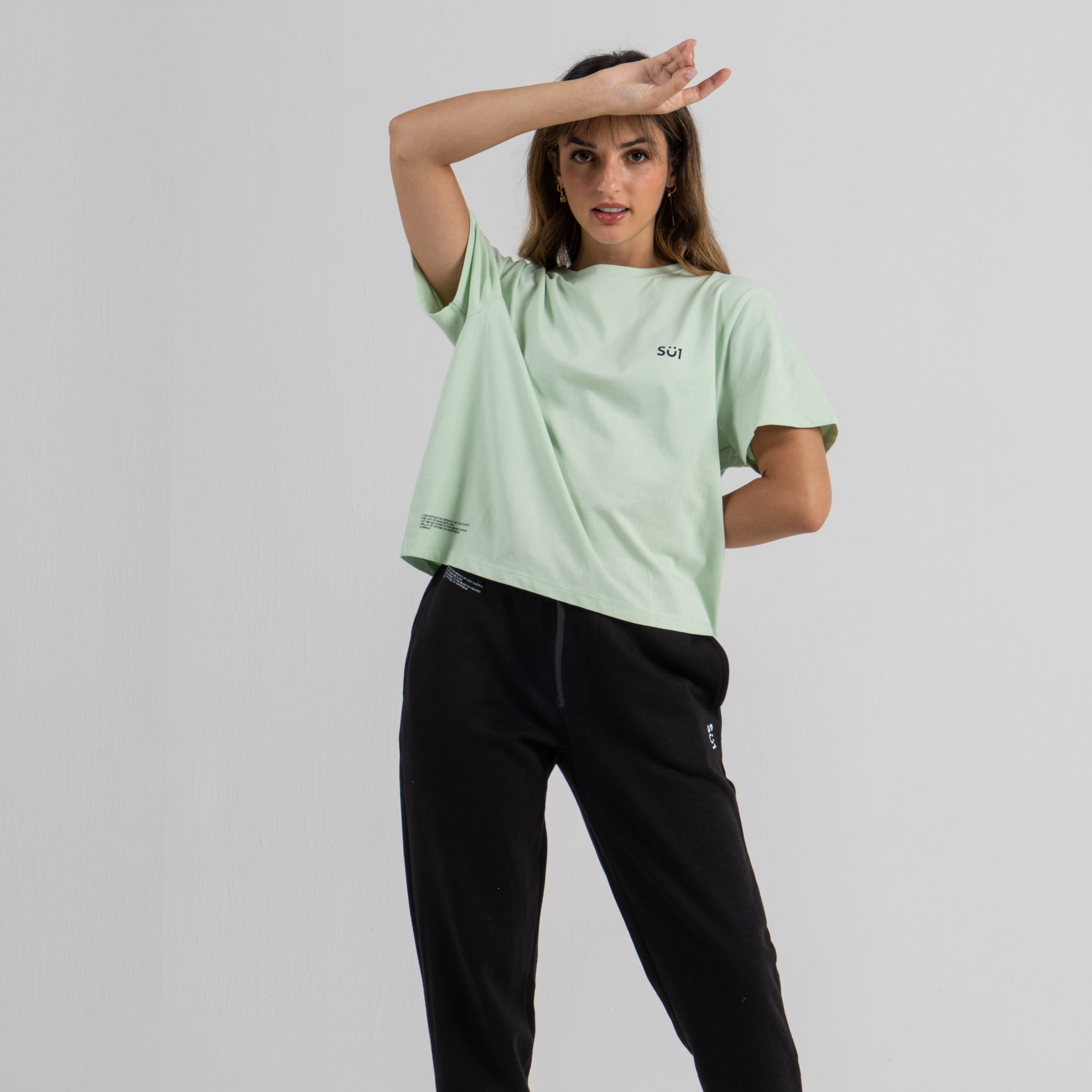 Woman wearing mint green mid crop tshirt SU1 clothing brand and black sport trousers