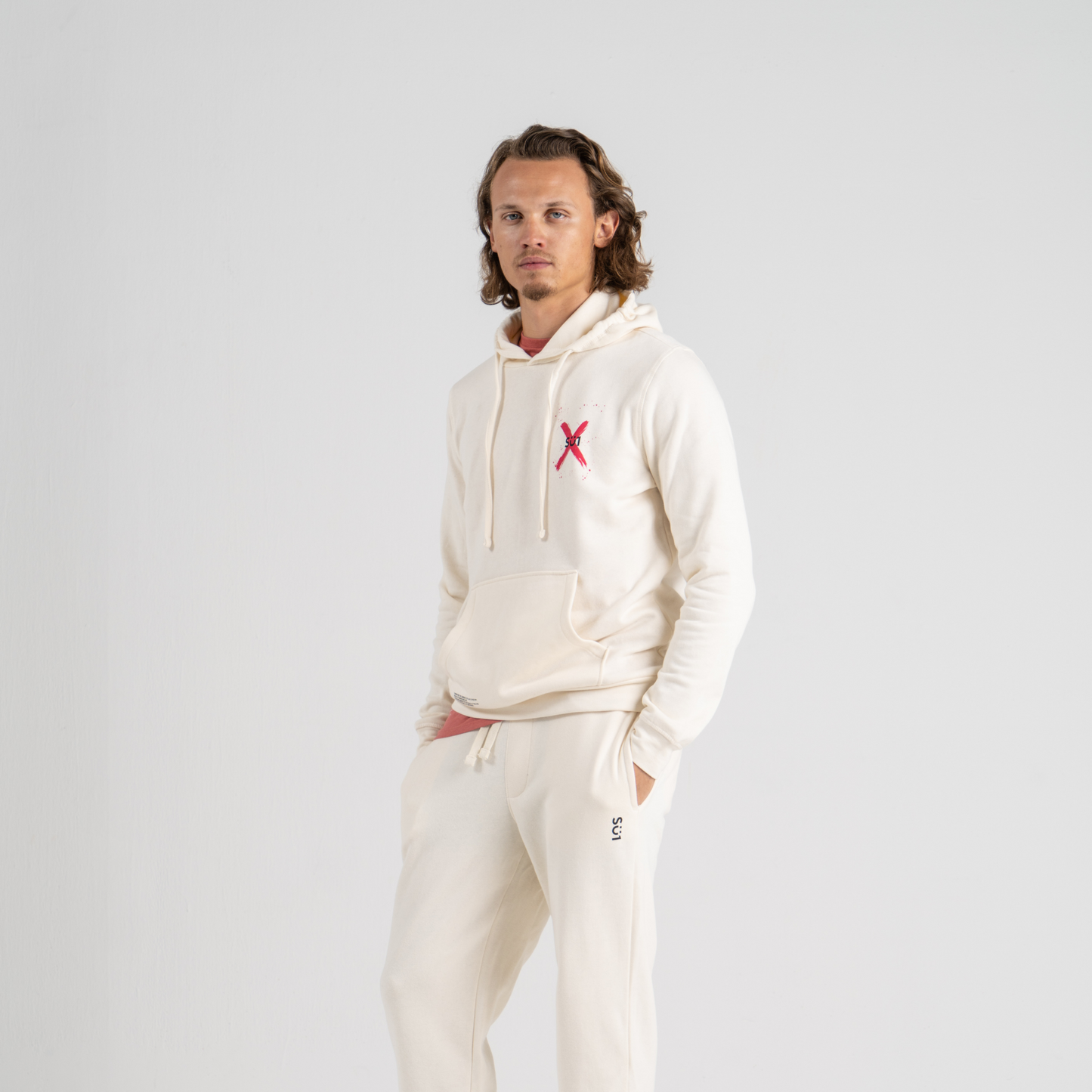 Man wearing ecru hoodie SU1 clothing brand and ecru sport trousers